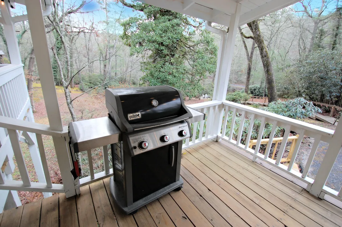 This image showcases a wooden deck with ample seating, a grill, and views of the surrounding greenery. The deck is spacious, inviting, and perfect for relaxing after a day on the trails. The setting highlights outdoor amenities where both guests and their dogs can unwind together safely.