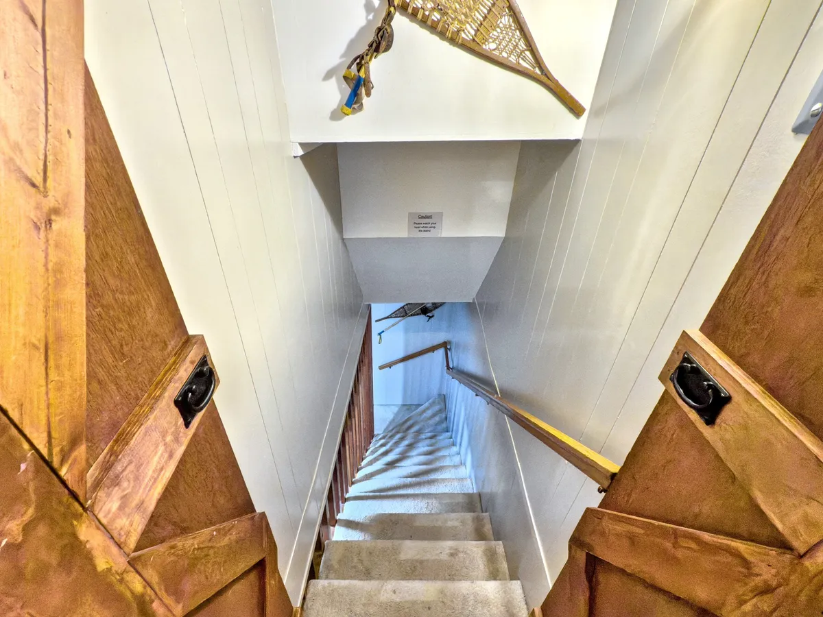 This image features a staircase with wooden doors and a snowshoe decoration on the wall, inviting guests to discover different levels of the home. The warm wood tones and cozy decor hint at the home's layered, welcoming design.