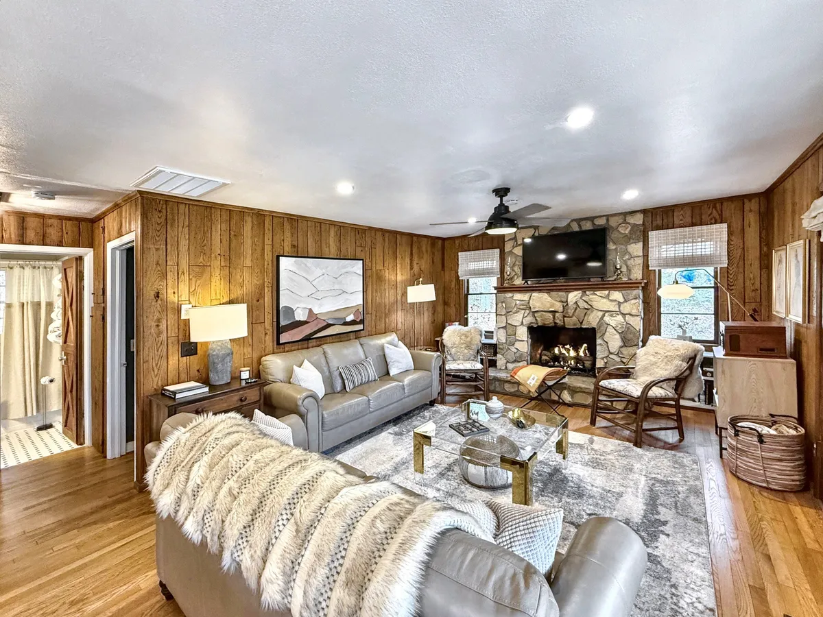 A welcoming living room featuring a prominent fireplace as the centerpiece, surrounded by a comfortable sofa, a patterned rug, stylish light fixtures, and tasteful artwork. The setting radiates warmth, making it ideal for both gatherings and relaxation.