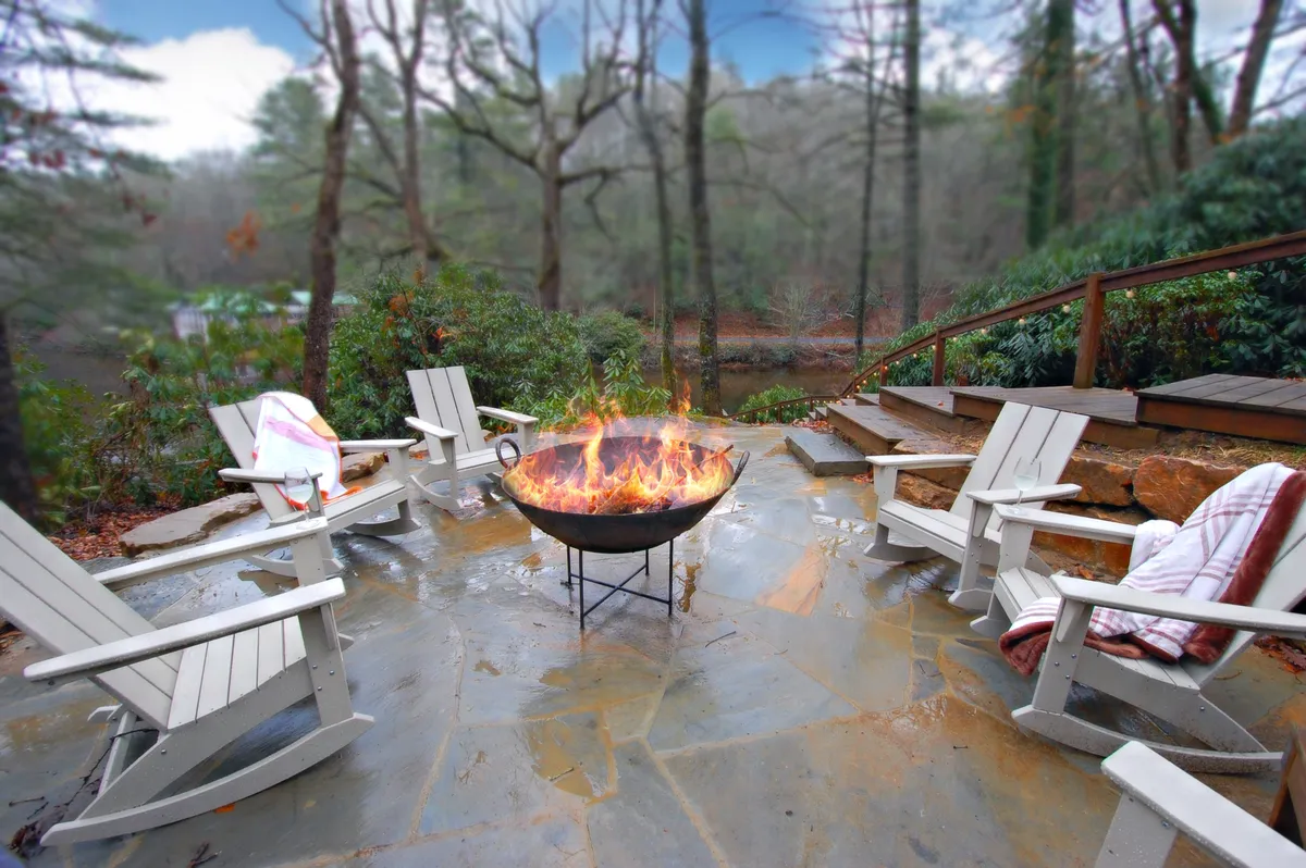A picturesque exterior setting features a fire pit with Adirondack chairs, surrounded by lush natural scenery. People are seen relaxing and enjoying the warmth of the fire, embodying the spirit of togetherness and shared adventure.