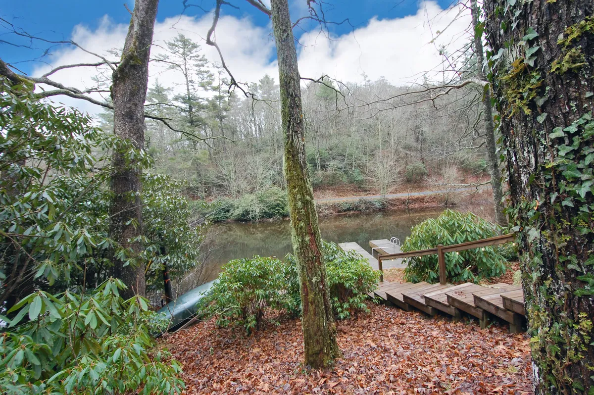 A tranquil riverside scene featuring a wooden set of steps leading down to the water, surrounded by lush trees and bushes. The water looks calm and inviting, ideal for canoeing or relaxing by the edge. This setting perfectly illustrates the direct access to the lake and the inviting nature of the outdoor adventure described in the section.