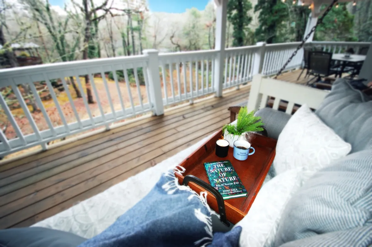 A wooden tray holding two cups and a book titled 'The Nature of Nature' rests outdoors, suggesting a serene spot for enjoying coffee and reading while surrounded by the sights and sounds of nature.
