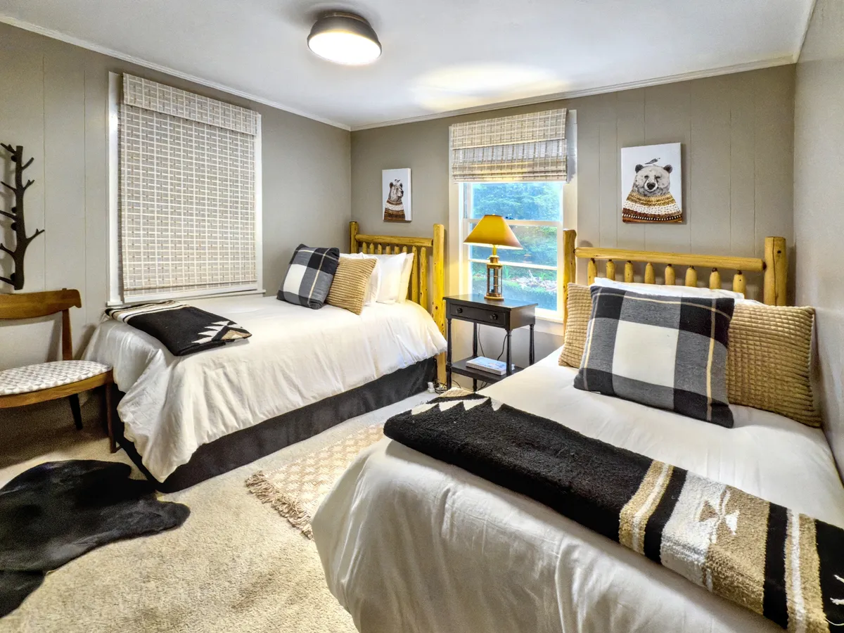 A cozy bedroom with two twin beds separated by a nightstand and lamp, complemented by decorative wall art. The room exudes a comfortable, homey atmosphere suitable for children or friends sharing a space.