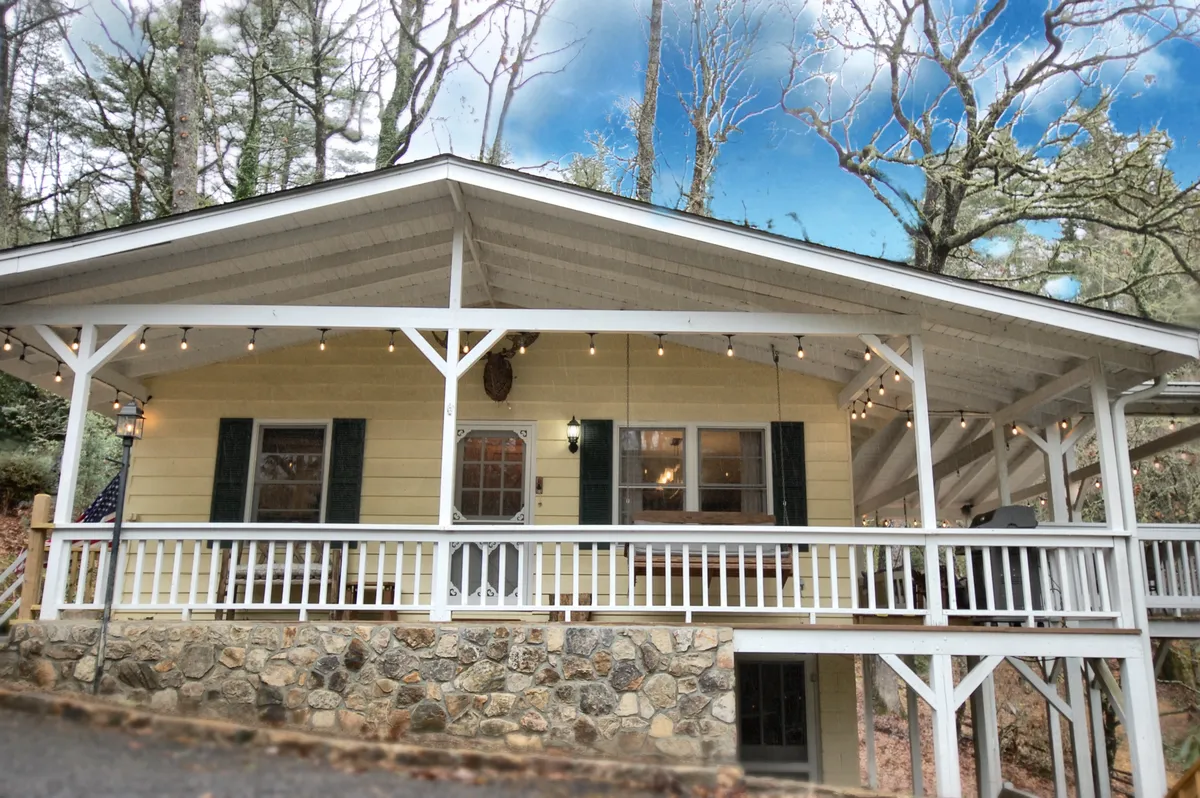 A welcoming porch with string lights, a stone foundation, wooden railings, and a front door. The atmosphere is cozy and inviting, ideal for gatherings or quiet moments in the evening.