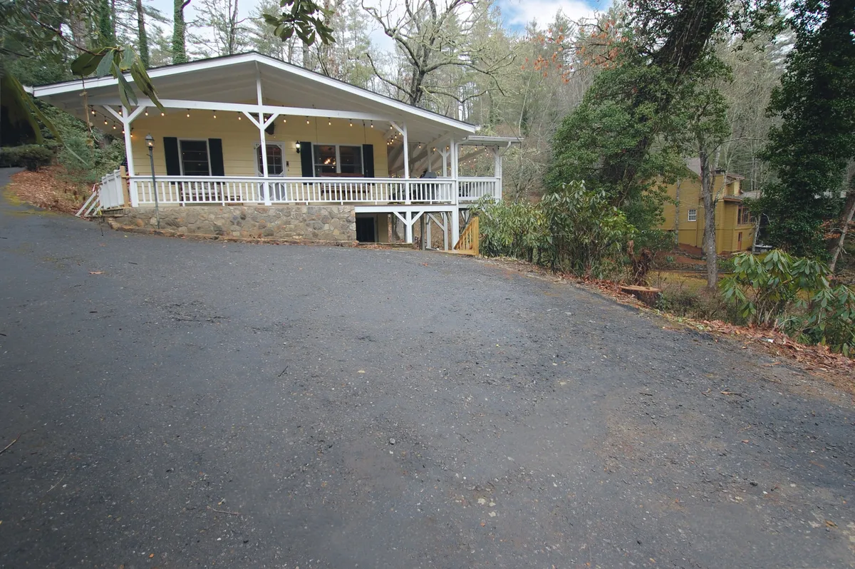 A welcoming porch with a railing and stone foundation, surrounded by tall trees. This exterior shot embodies relaxation, offering a peaceful spot to enjoy morning coffee or an after-work break immersed in nature.