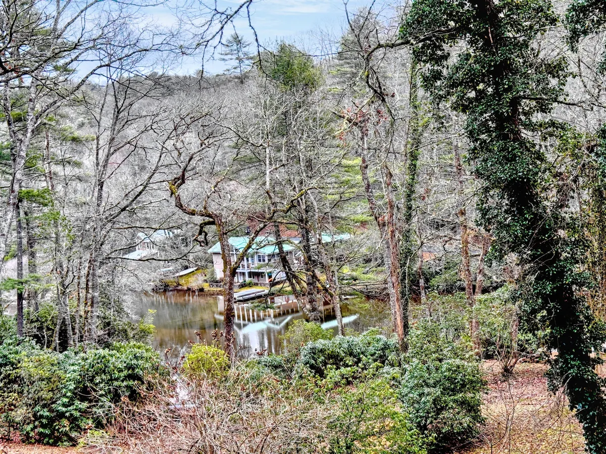 A beautiful lakeside view with a house nestled by the water, surrounded by trees. The still water reflects the landscape, and the overall mood is peaceful, hinting at activities like fishing, relaxing, or simply enjoying the lake's natural beauty.