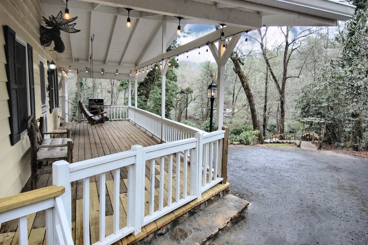 A peaceful exterior porch scene featuring a rocking chair, string lights, and surrounding trees. The cozy porch invites relaxation and offers a welcoming transition from the home to the outdoors, hinting at the proximity to local attractions.